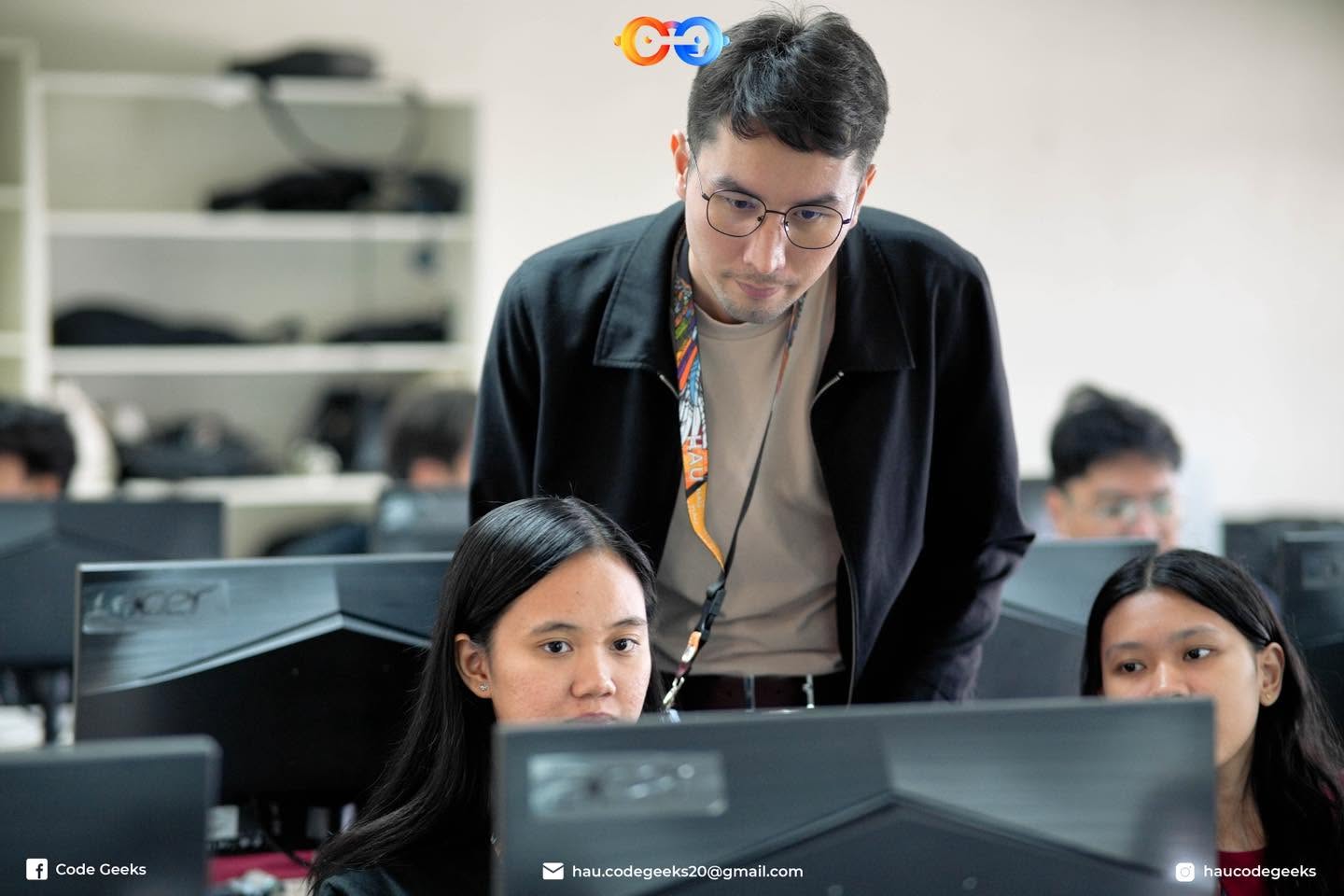 Me leaning over a student's station reading her screen, two more students working at the machines beside her