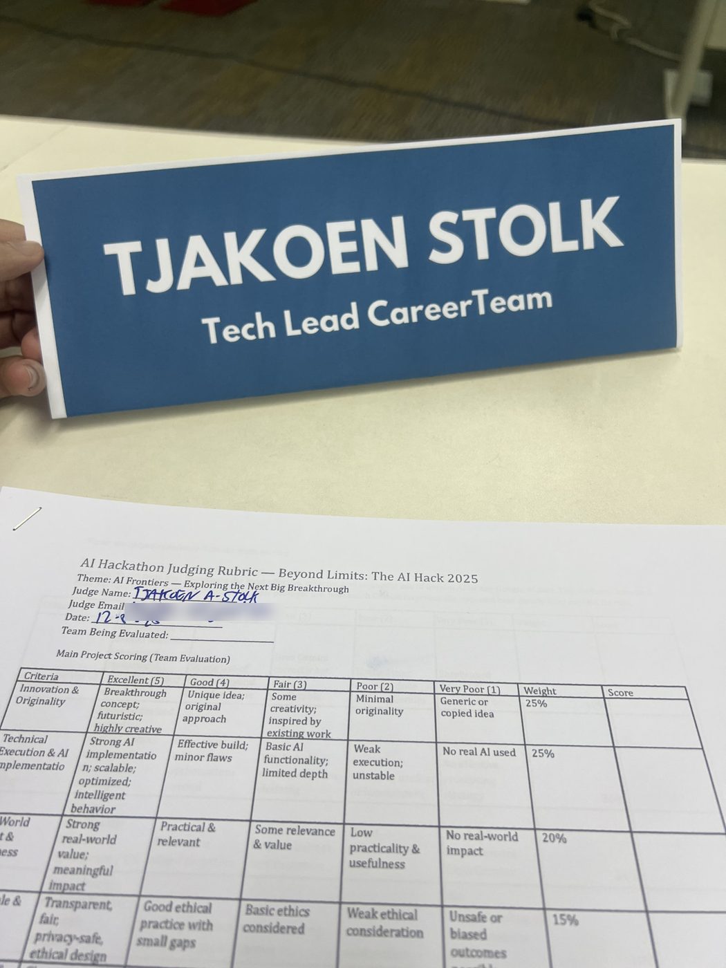 The judging sheet before the first team went up: five criteria, weights running from 25 percent down to 15, my name in the blank at the top and my email blurred out under it