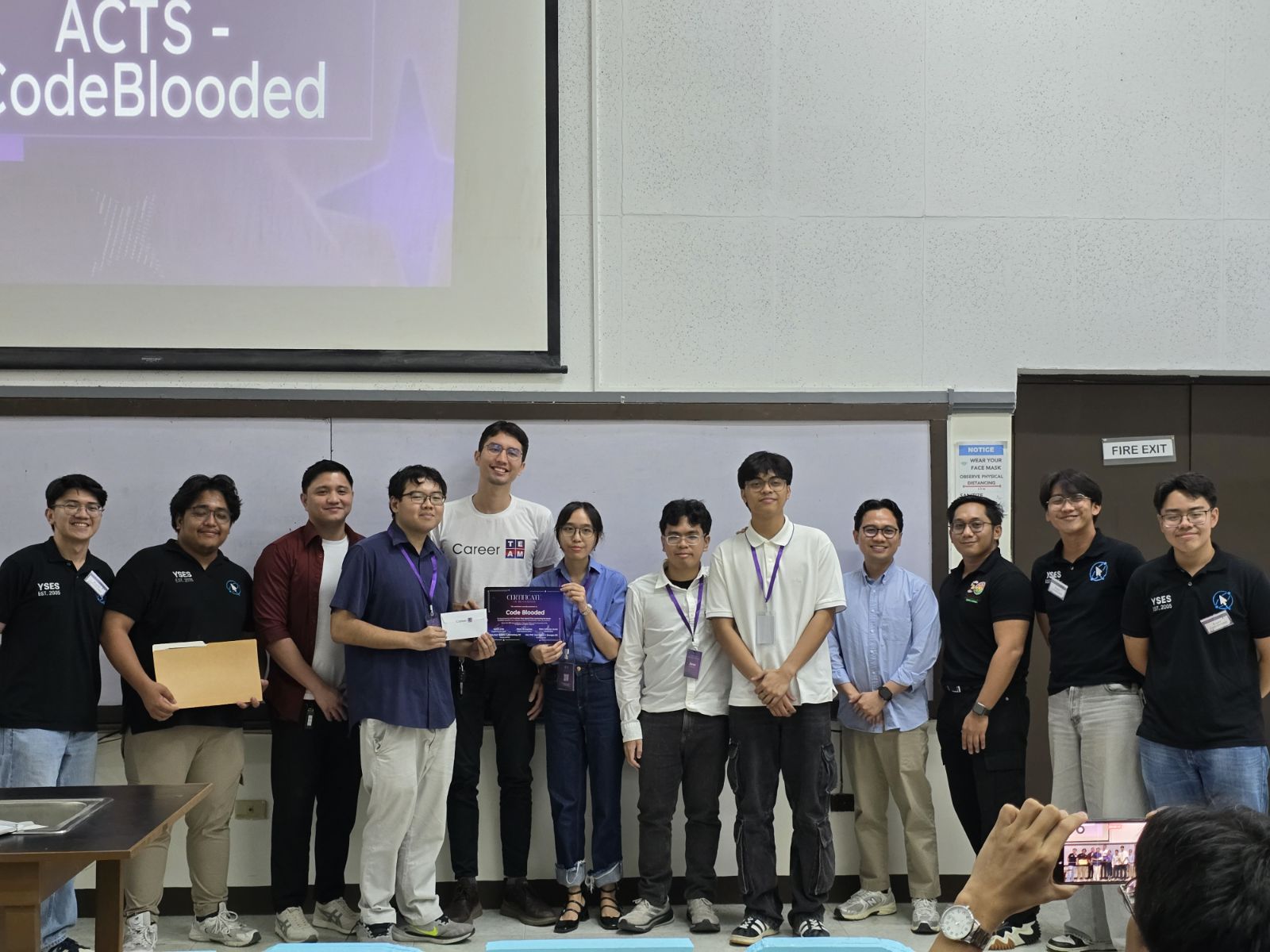 Team CodeBlooded with the organizers and judges after the award, the projector still showing their title slide, ACTS
